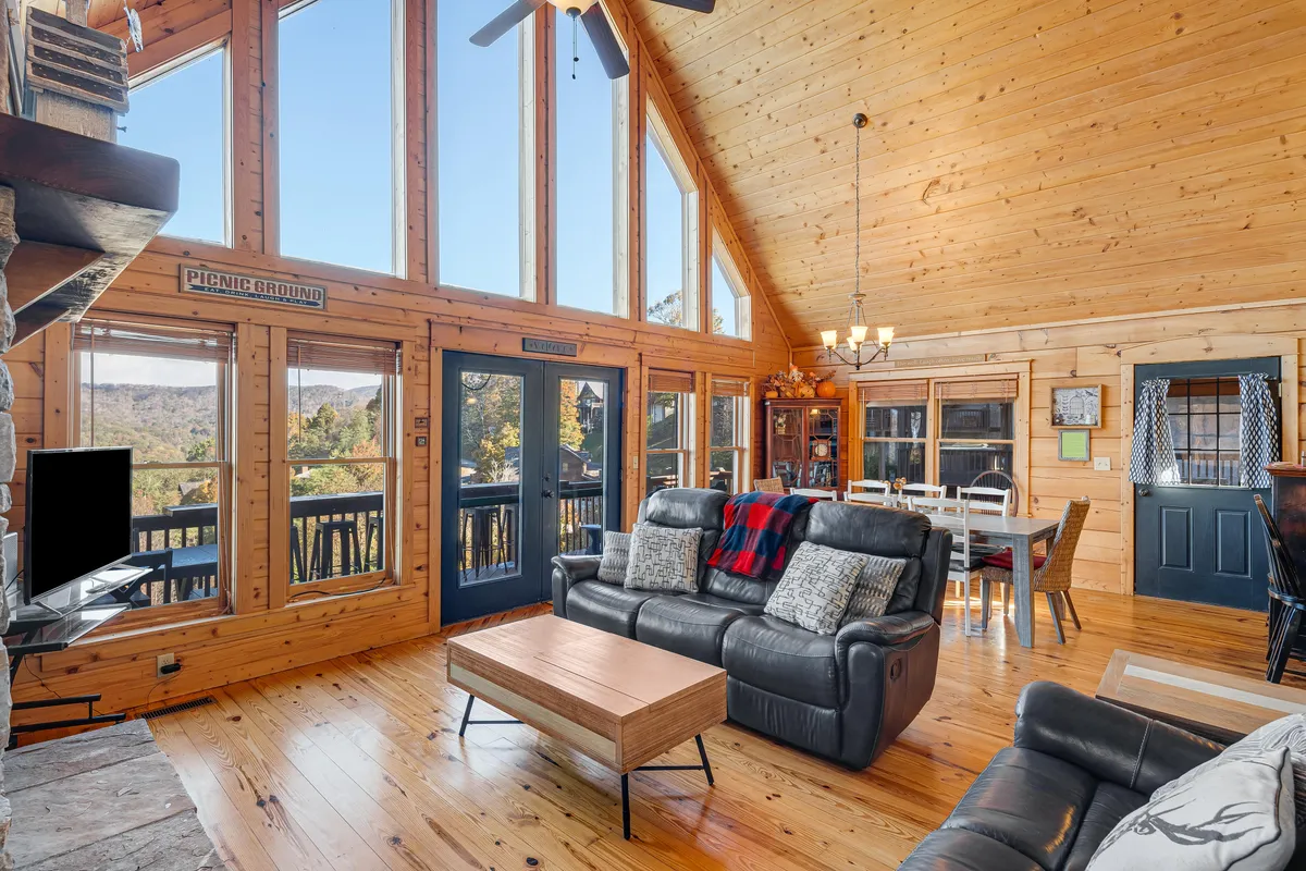 A broad view of an open-plan living and dining area with comfortable leather sofas, wooden beams, and expansive windows that offer panoramic mountain vistas. The space encourages connection and conversation, blending relaxation with opportunities to take in the natural setting.
