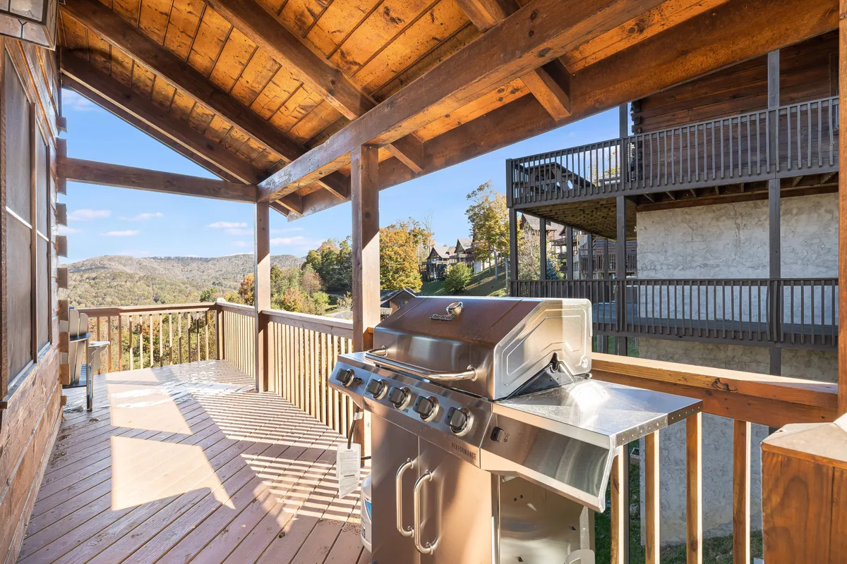 A spacious wooden deck features an outdoor grill, bar area, and sweeping mountain vistas. The setup invites guests to enjoy morning coffee, al fresco dining, and evening toasts with nature as the backdrop.