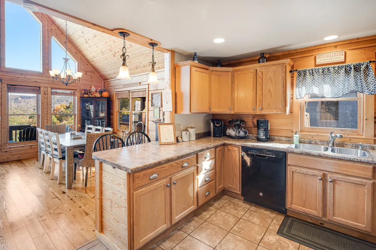 This image captures the heart of the home, showing a spacious kitchen counter and a large dining table set against the backdrop of expansive windows. Natural light pours in, illuminating a welcoming space perfect for preparing meals or gathering for family dinners. The view through the windows hints at the scenic mountain landscape outside, seamlessly blending comfort with inspiration.