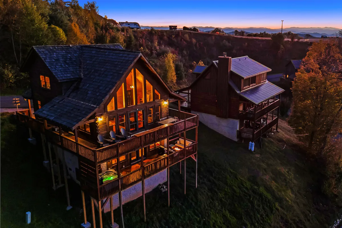 A large wooden deck with spacious windows overlooks the Blue Ridge Mountains, surrounded by towering trees. The deck is set up for outdoor dining and family gatherings, with plenty of space for kids to play and adults to relax. The serene, cozy atmosphere hints at both nature exploration and comfortable evenings together.