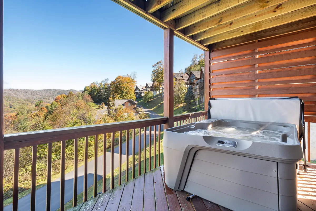 A steaming hot tub sits on a wooden deck overlooking a vast mountain panorama, with a serene sky in the background. The space is designed for relaxation and socializing after a day of outdoor exploration.
