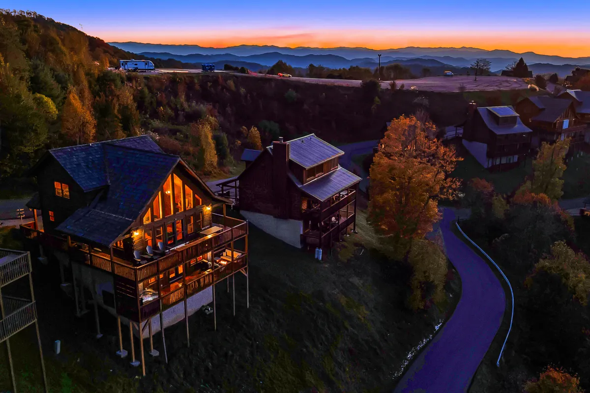 The image showcases a wooden cabin nestled against a dramatic mountain landscape during a vibrant sunset. The scene radiates a private, secluded atmosphere ideal for a romantic escape.