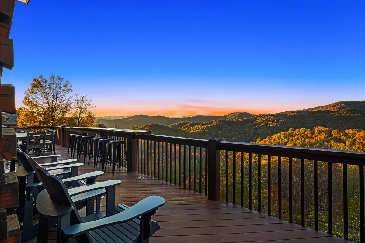 This image captures a serene deck with comfortable seating, overlooking sweeping mountain views under a glowing sunset sky. The deck setting is inviting for relaxation, stargazing, and sharing special moments as a couple.