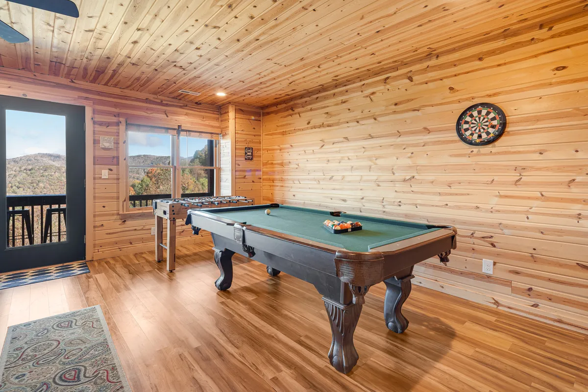 A lively game room filled with a pool table, foosball table, and dartboard set against large windows. The space is bright and inviting—ideal for friendly family competitions and winding down after a day outdoors.